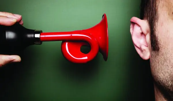 A red megaphone is held close to a person's ear against a green background.