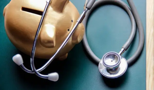 A golden piggy bank is juxtaposed with a stethoscope against a green background, symbolically representing the concept of financial health or the costs associated with medical care.