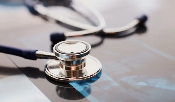 A stethoscope lies on a reflective surface alongside what appears to be a printed graph, suggesting a medical or healthcare setting.