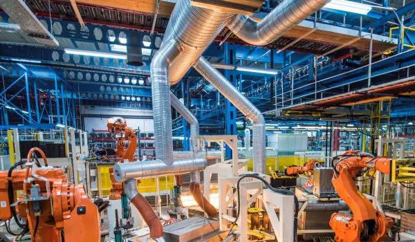 A modern industrial facility equipped with orange robotic arms and machinery, with a complex network of pipes overhead.