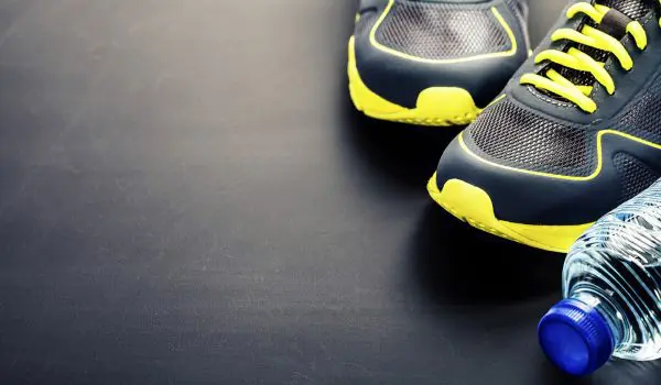 Pair of blue and yellow athletic shoes beside a plastic water bottle on a dark surface.