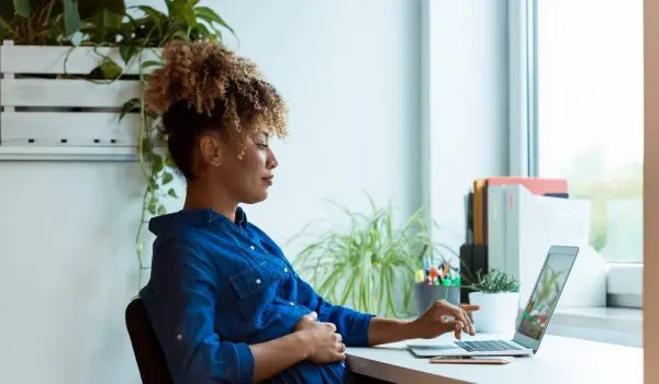 A person is working on a laptop at a desk with plants and office supplies nearby.