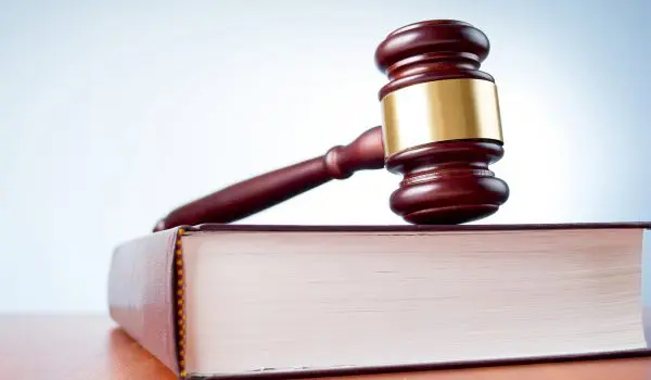 A gavel rests atop a closed book on a flat surface.