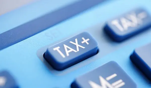 A close-up view of a blue calculator with a "TAX+" button prominently displayed.