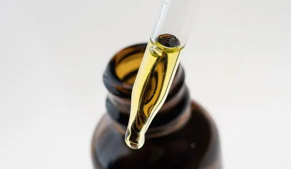 A droplet of yellow liquid is suspended from a dropper above an open brown bottle.