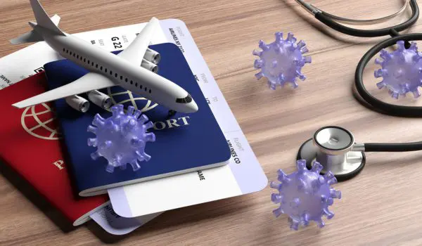 A model airplane, passports, stethoscope, and virus illustrations are arranged on a wooden surface.