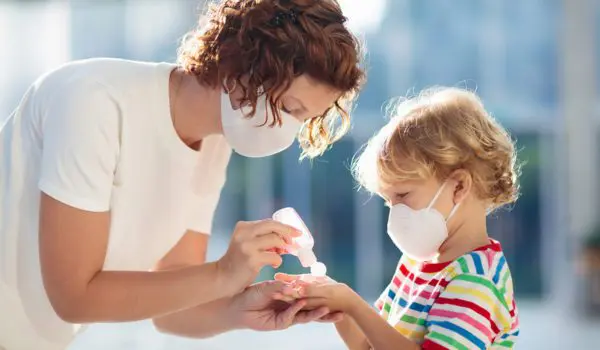 An adult is helping a child use hand sanitizer, and both are wearing masks.