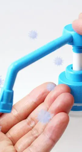 A person is using a hand sanitizer dispenser while surrounded by illustrated virus particles.