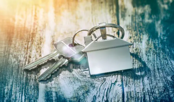 House keys with a keychain shaped like a house lie on a rustic wooden surface.