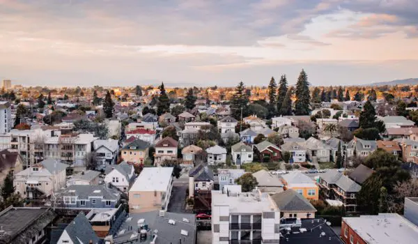 An aerial view showcases a suburban neighborhood with a mix of houses and trees under a partly cloudy sky.