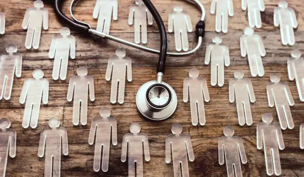 A stethoscope is laid over a wooden surface surrounded by transparent human figure cutouts.