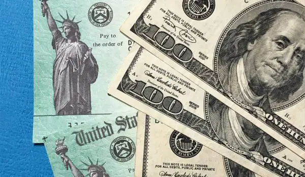 Several 100-dollar bills are placed on top of documents that appear to be U.S. Treasury checks.