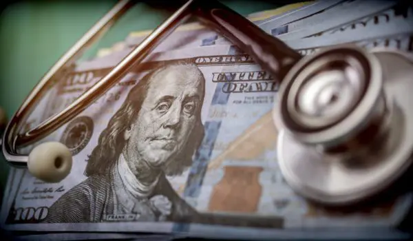 A stethoscope rests on top of several U.S. hundred-dollar bills.