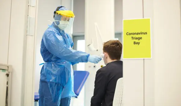 A healthcare worker in full protective gear is conducting a coronavirus test on a seated individual in a designated triage bay.