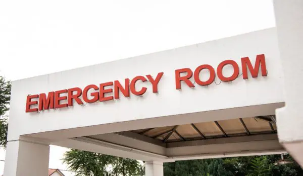 Sign for an emergency room entrance with trees and buildings in the background.
