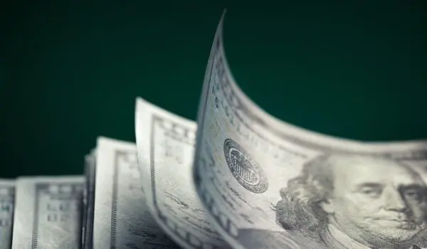 A stack of U.S. one hundred dollar bills with the top bill slightly curled.