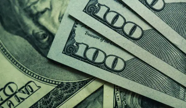 Several 100-dollar bills are fanned out, showing Benjamin Franklin's portrait.