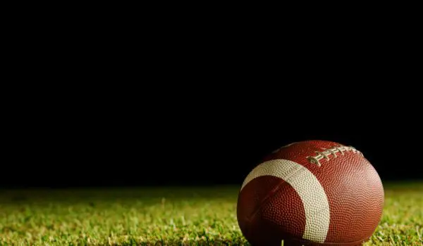 A football rests on a grassy field against a dark background.