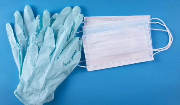 Blue medical gloves and white face masks are arranged on a blue surface.