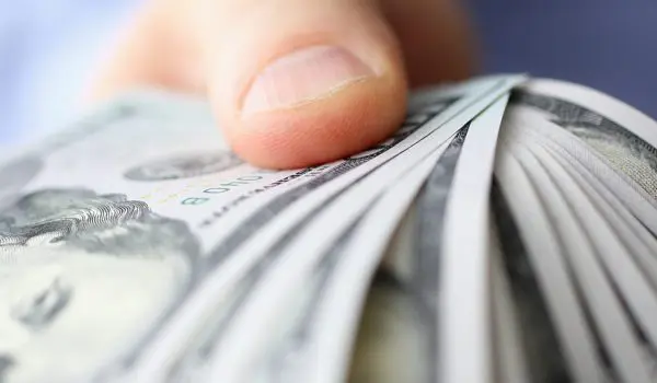 A hand is holding a fanned-out stack of US dollar bills.