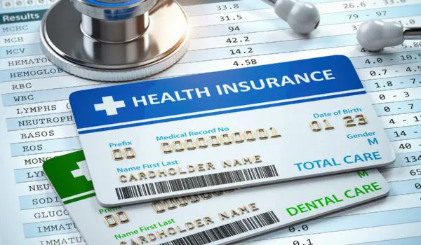 Three health insurance cards and a stethoscope lie on top of a medical billing statement.
