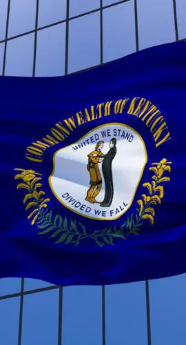 A Kentucky state flag is waving in front of a glass building.