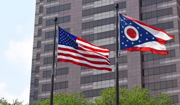 Two flags, one of the United States and one of Ohio, are flying in front of a tall building.