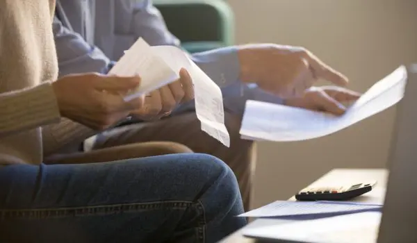 Two individuals are reviewing papers and receipts, with a calculator and a laptop nearby.