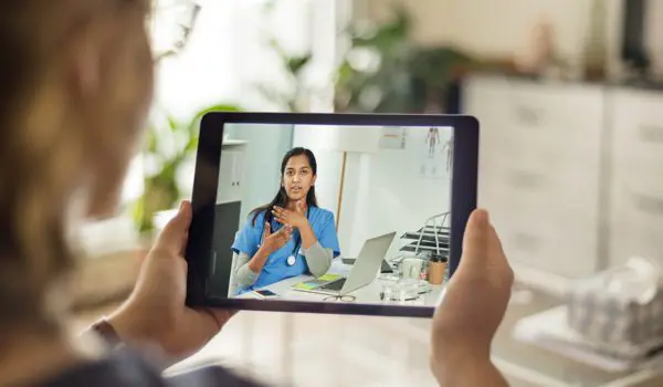 Someone is holding a tablet displaying a virtual medical consultation with a healthcare professional.