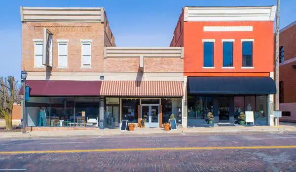 Two storefronts, one with a red brick facade and the other with a light brown brick facade, are visible along a paved street.