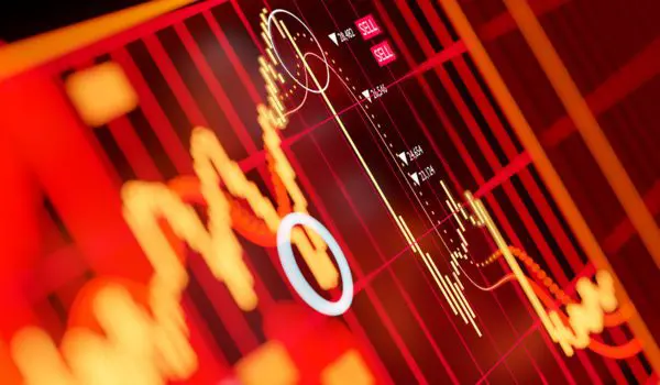 A red-dominated screen displays fluctuating financial stock or market data with graphs and charts.