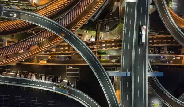A complex network of illuminated highways and overpasses is captured from an aerial perspective at night.
