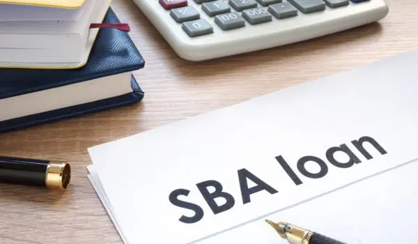 A document labeled "SBA loan" is on a desk next to a pen, some notebooks, and a calculator.