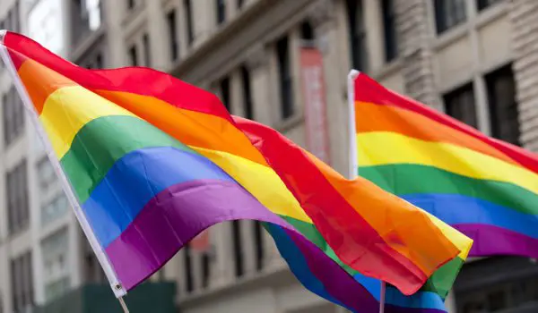 Rainbow flags are waving in front of a series of beige buildings.