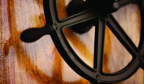 A ship's steering wheel mounted on a wooden surface with soft lighting highlighting its texture.