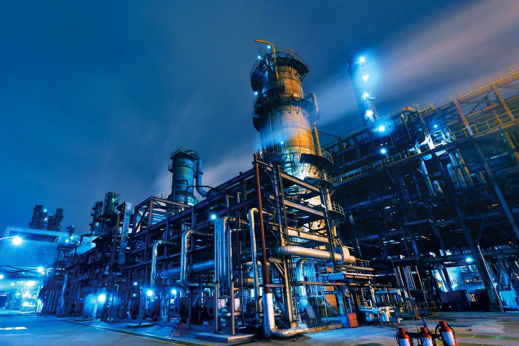 An industrial complex with steel structures is illuminated at night, showcasing the operation of what appears to be a chemical or power plant.
