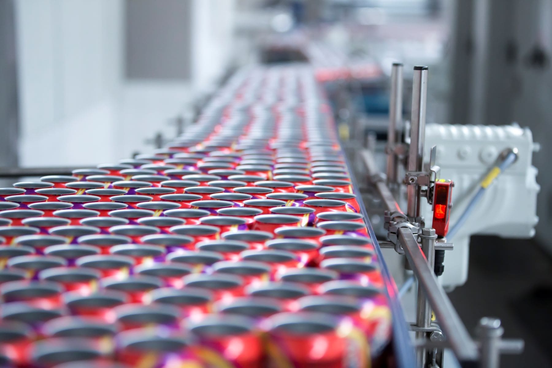 A conveyor belt with rows of red aluminum cans in a manufacturing facility.