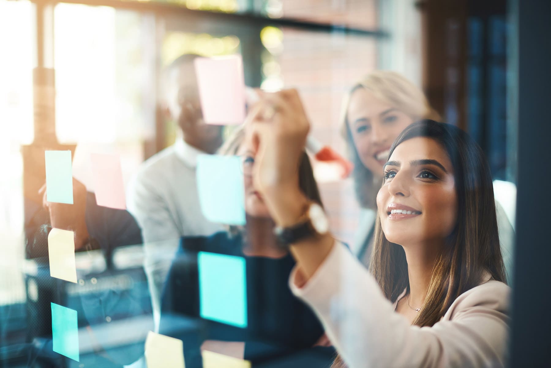 A group of professionals is engaged in a collaborative brainstorming session with sticky notes on a glass window.