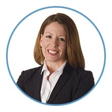 A smiling person is wearing a white shirt and dark blazer, framed within a blue circle.