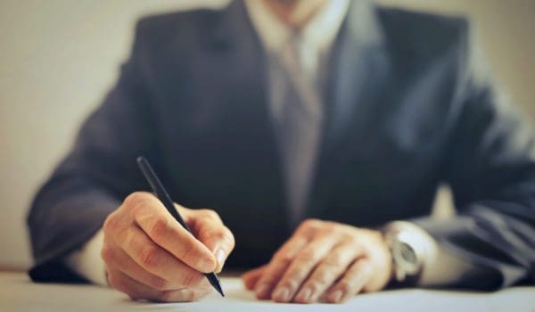 Crop businessman signing contract in office