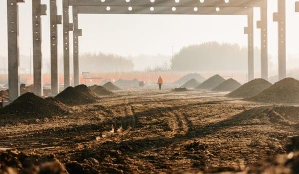 An industrial construction site under a large, unfinished structure with mounds of soil and metal framework.