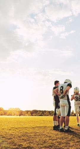 Group of young American football players standing together in a circle on a sports field talking strategy