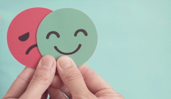 Hands holding sad face hiding behind happy face, bipolar and depression, mental health, split personality,  mood change,