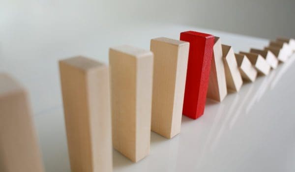 Close-up of one red wooden block stop other ones from falling like dominoes, domino effect. Risky and business strategy, planning, danger, fail concept