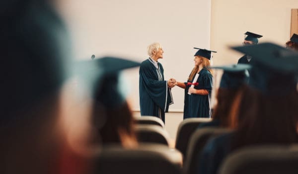 Happy senior professor shaking hands with her graduate students in a lecture hall. Copy space.