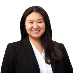 A person with long, dark hair is smiling while wearing a black blazer and a white top against a plain white background.