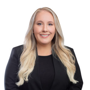 A blonde woman is smiling while wearing a black blazer against a white background.