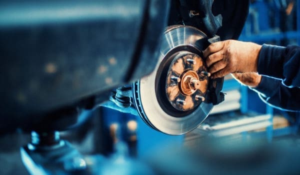 Closeup of unrecognizable mechanic replacing car brake pads. The car is lifted with hydraulic jack at eye level.