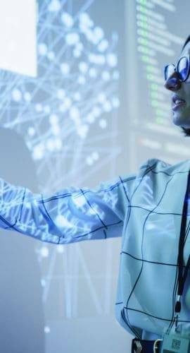 Young Female Teacher Giving a Data Science Presentation in a Dark Auditorium with Projecting Slideshow with Artificial Intelligence Neural Network Architecture. Business Startup and Education Concept