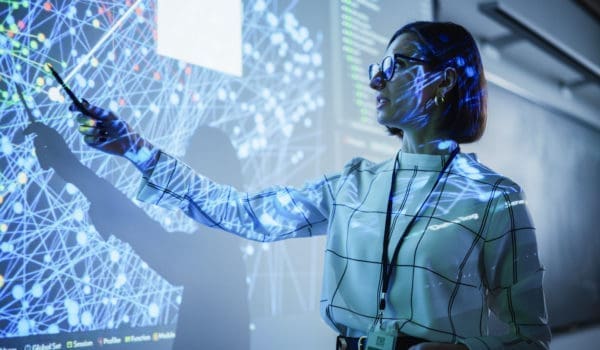 Young Female Teacher Giving a Data Science Presentation in a Dark Auditorium with Projecting Slideshow with Artificial Intelligence Neural Network Architecture. Business Startup and Education Concept